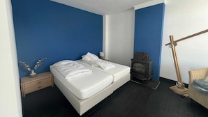 A bedroom with a double bed, a nightstand, a dresser, a wooden floor, a wall heater, and a wicker chair. - Unique House Within Walking Distance of the Beach (Katwijk Aan Zee)