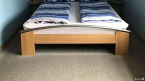 A single bed with a wooden frame and a headboard, positioned in a room with light blue walls and a sloped ceiling. - Holiday Apartment Hinrichsen 2 (Midlum)