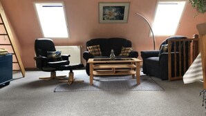 A cozy living room with a black sofa, a wooden coffee table, and a black armchair. There are two windows providing natural light, and a painting hangs on the wall. - Holiday Apartment Hinrichsen 2 (Midlum)