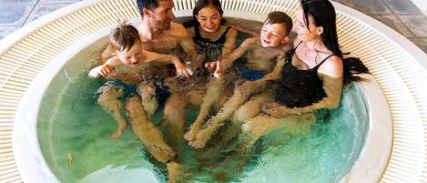 Un groupe de personnes dans un jacuzzi, avec un sol carrelé et un mur blanc en arrière-plan.