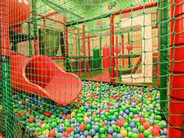 Un área de juegos con un tobogán rojo y un foso de pelotas lleno de bolas multicolores.
