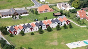 A row of uniform houses with red roofs and white walls, a grassy area, and a swimming pool.