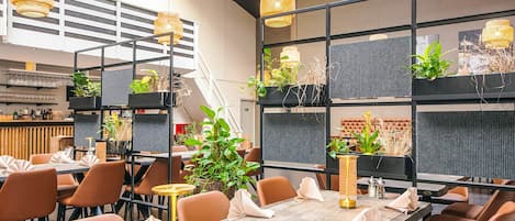 Un restaurant moderne avec de longues tables, des chaises orange et des lampes en osier suspendues au plafond.