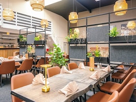 A modern restaurant with long tables, orange chairs, and hanging wicker lamps.