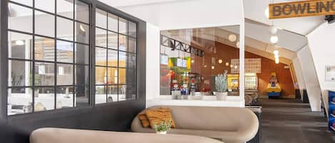 A modern interior with a sofa, a large window, and a sign reading 'BOWLING'.