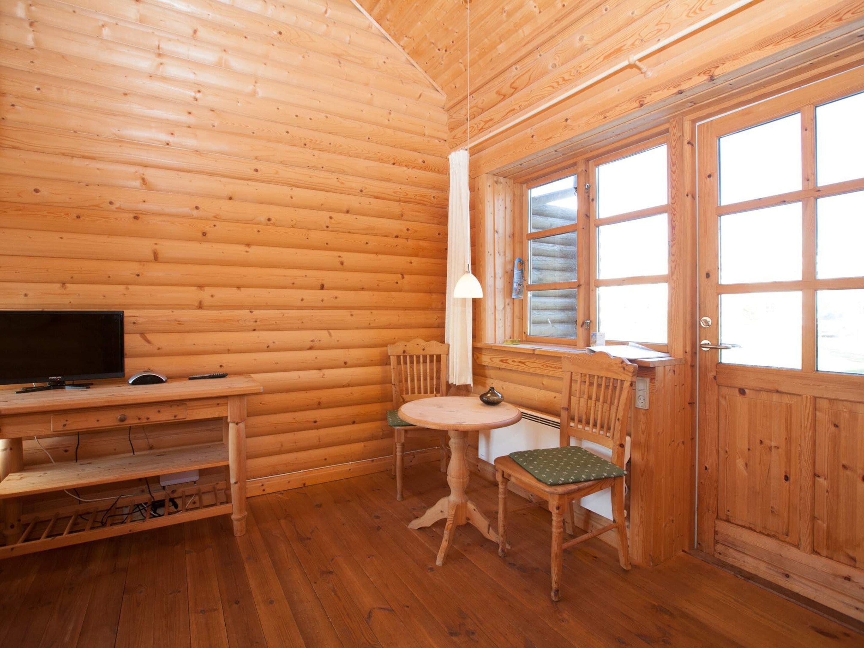 L’intérieur d’un chalet en bois, avec un téléviseur, une table, deux chaises et une fenêtre.