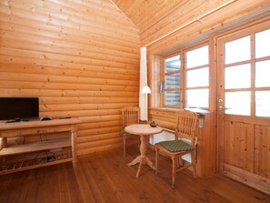 Interior d'una cabana de fusta amb un televisor, una taula, dues cadires i una finestra.