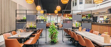 A modern restaurant with high tables, orange chairs, and hanging wicker lamps.