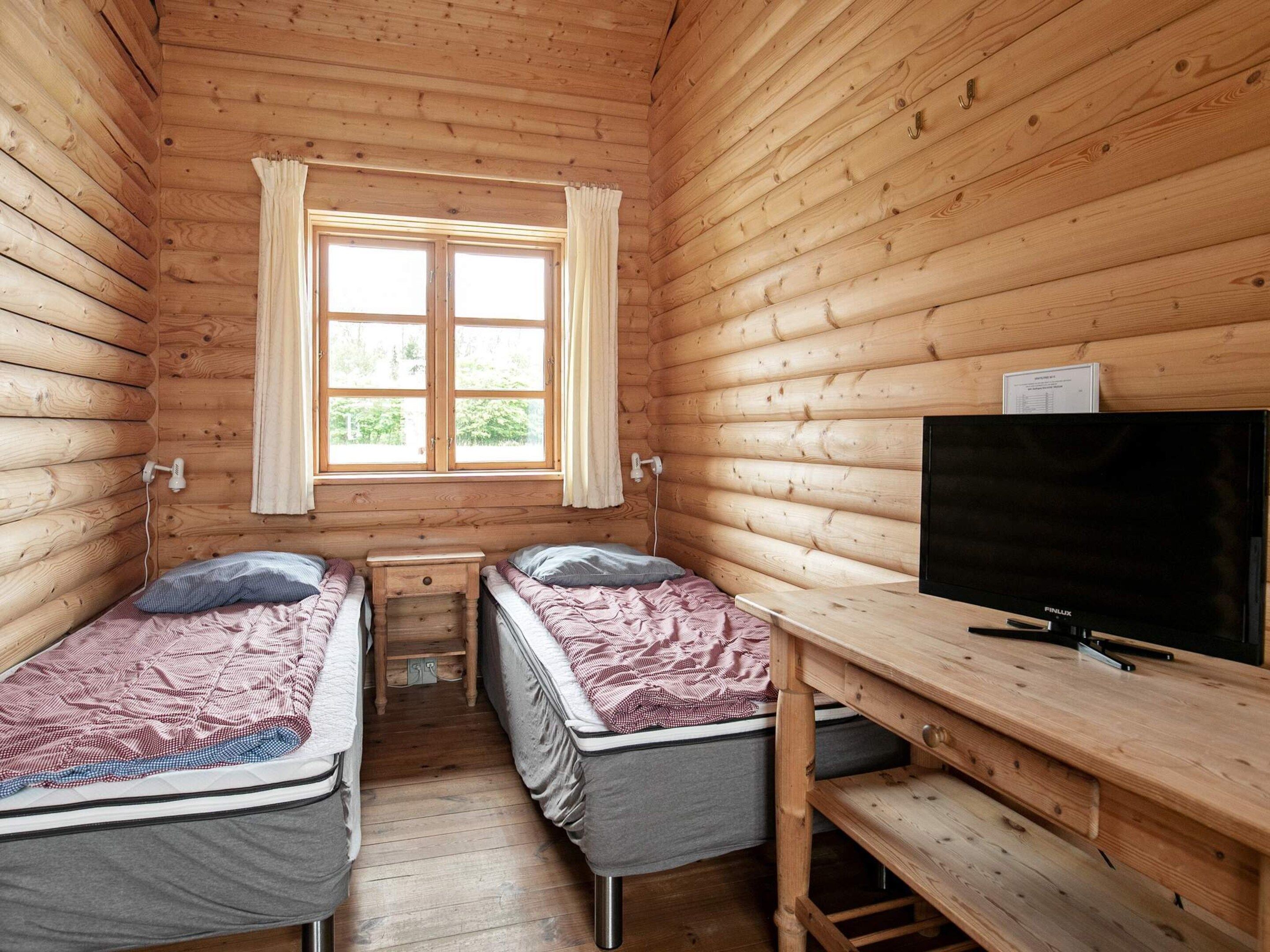 A cabin with two single beds, a wooden desk, a television, and a window with curtains.