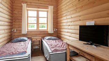 A cabin with two single beds, a wooden desk, a television, and a window with curtains.