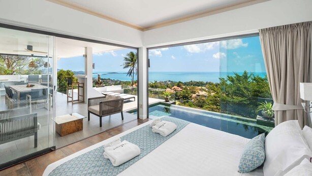 A modern hotel room with a large bed, a glass-enclosed balcony, a dining area, and a view of the ocean. - Serene Escape Villa in Chaweng - KBR20 (Koh Samui)