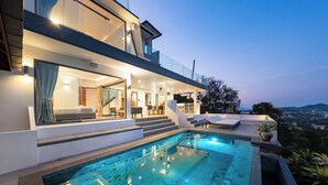 A modern house with a swimming pool, outdoor seating, and a view of the city at dusk. - Serene Escape Villa in Chaweng - KBR20 (Koh Samui)