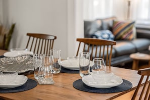 A dining table set with clear glassware and plates, wooden chairs, and a patterned placemat. - Sailors Aweigh: Marblehead 3BR Retreat with Outdoor Space Near Harbor & Beaches (Marblehead)