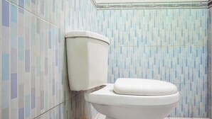A toilet with a white seat and lid, set against a wall with a geometric tile pattern.