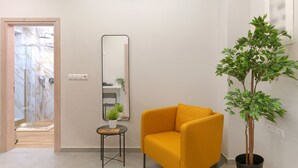 A modern living room with a yellow armchair, a potted plant, and a mirror on the wall.