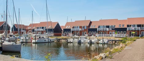 En småbåtshamn med förtöjda båtar, en träbrygga och en rad hus med röda tak.