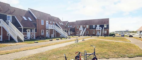 Une rangée d’immeubles en briques, dotés d’escaliers extérieurs et bordée d’un chemin de gravier.