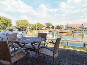 Eine Holzterrasse mit Korbstühlen und einem Tisch mit Blick auf eine Marina, im Hintergrund Boote und Gebäude.