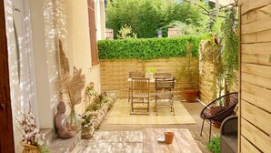 En terrasse med et bord, stole, en Buddha-figur og plantekrukker.