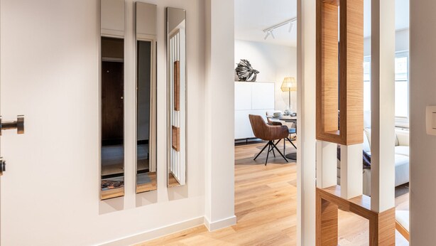 Un interior moderno con piso de madera, un área de comedor con mesa y sillas, y una cocina al fondo.