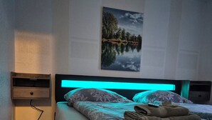 A bedroom with a bed, a nightstand, a wall-mounted painting, and a wooden floor.