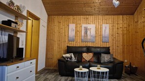 A cozy living room with a wooden ceiling, a black leather sofa, and two round side tables.
