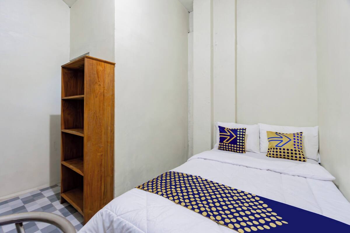 Un dormitorio pequeño y ordenado con una cama individual, un armario de madera y un suelo a cuadros.