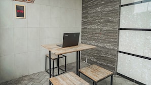 Ein kleiner Arbeitsbereich mit einem Laptop auf einem Holztisch, einem gerahmten Schild an der Wand und einem Fliesenboden.