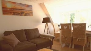 A cozy living room with a brown sofa, a small round table, wicker chairs, a floor lamp, and a painting of a sunset. - Holiday Apartment Strandkrabbe (Ockholm)