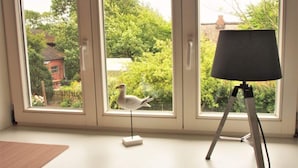 A room with a large window, a white desk, and a lamp on a tripod stand. - Holiday Apartment Strandkrabbe (Ockholm)