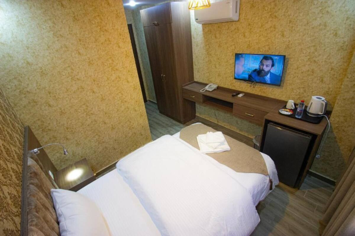 A hotel room with a bed, a desk with a telephone, a television, and a small refrigerator.