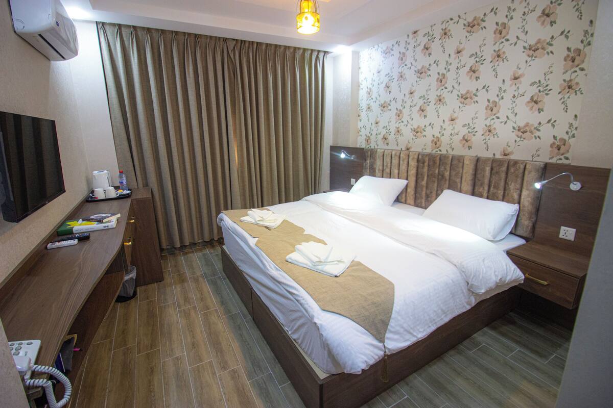 A hotel room with a large bed, a TV, a desk with a computer, and a bathroom.