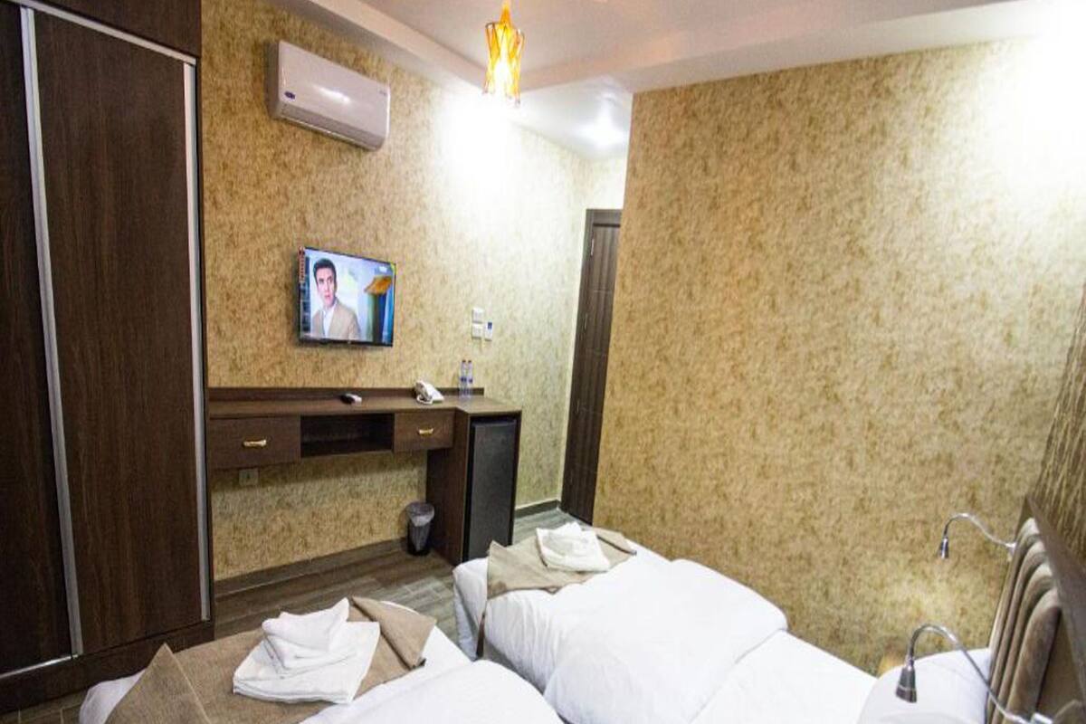 A hotel room with two beds, a desk, a TV, and an air conditioning unit.