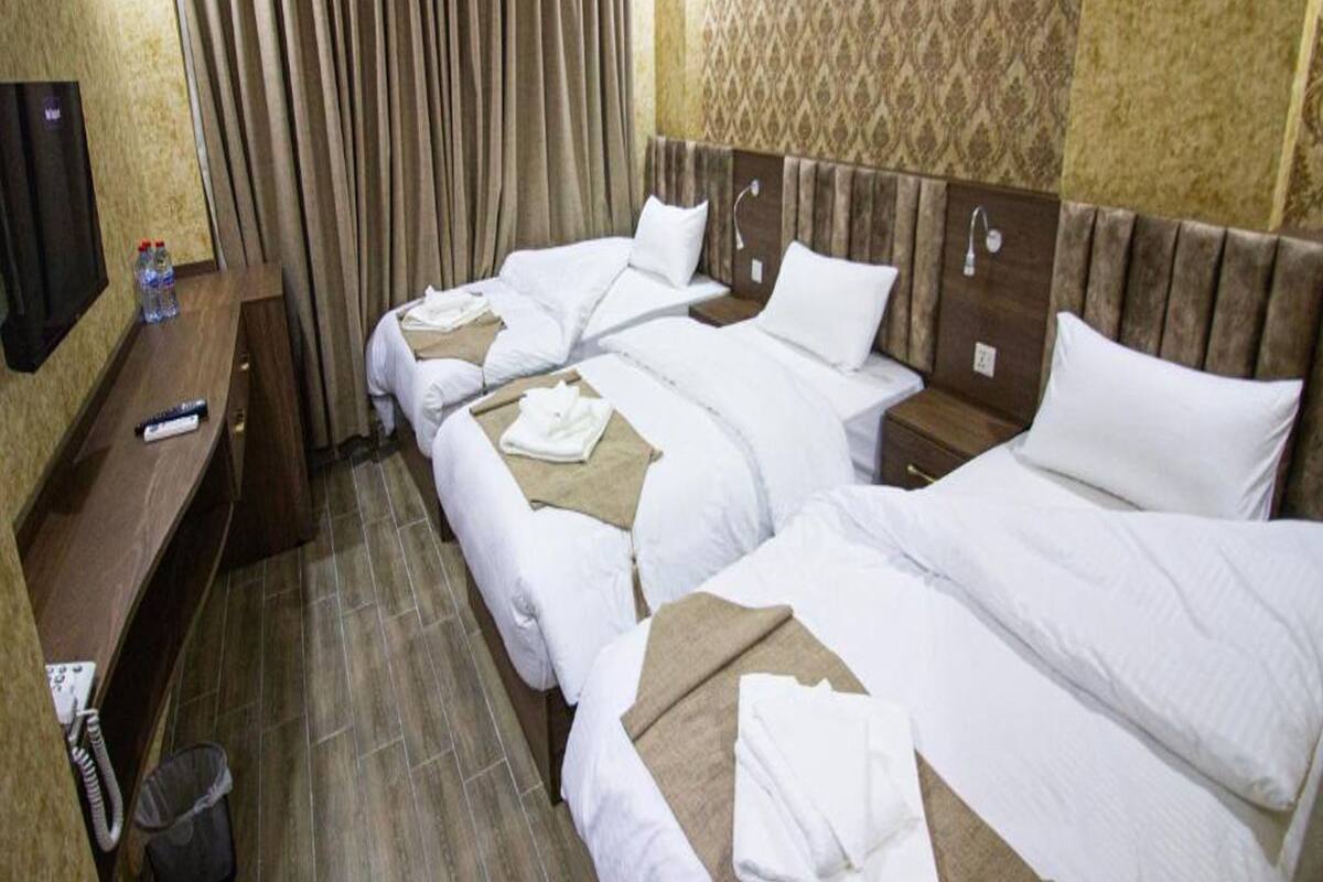 A hotel room with two beds, a desk, a TV, and a curtain.