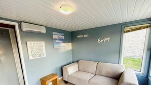 A room with a beige sofa, a wooden stool, and a wall with motivational quotes. - Lovely Holiday Home in Vlaanderen With Garden (De Haan)