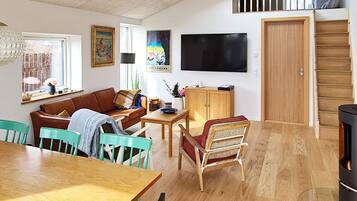 Ein Wohnzimmer mit einer Couch, Sesseln, einem Tisch, einem Fernseher und einer Holztür.