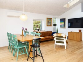 A modern living room with a dining area, a sofa, a television, and a large window.
