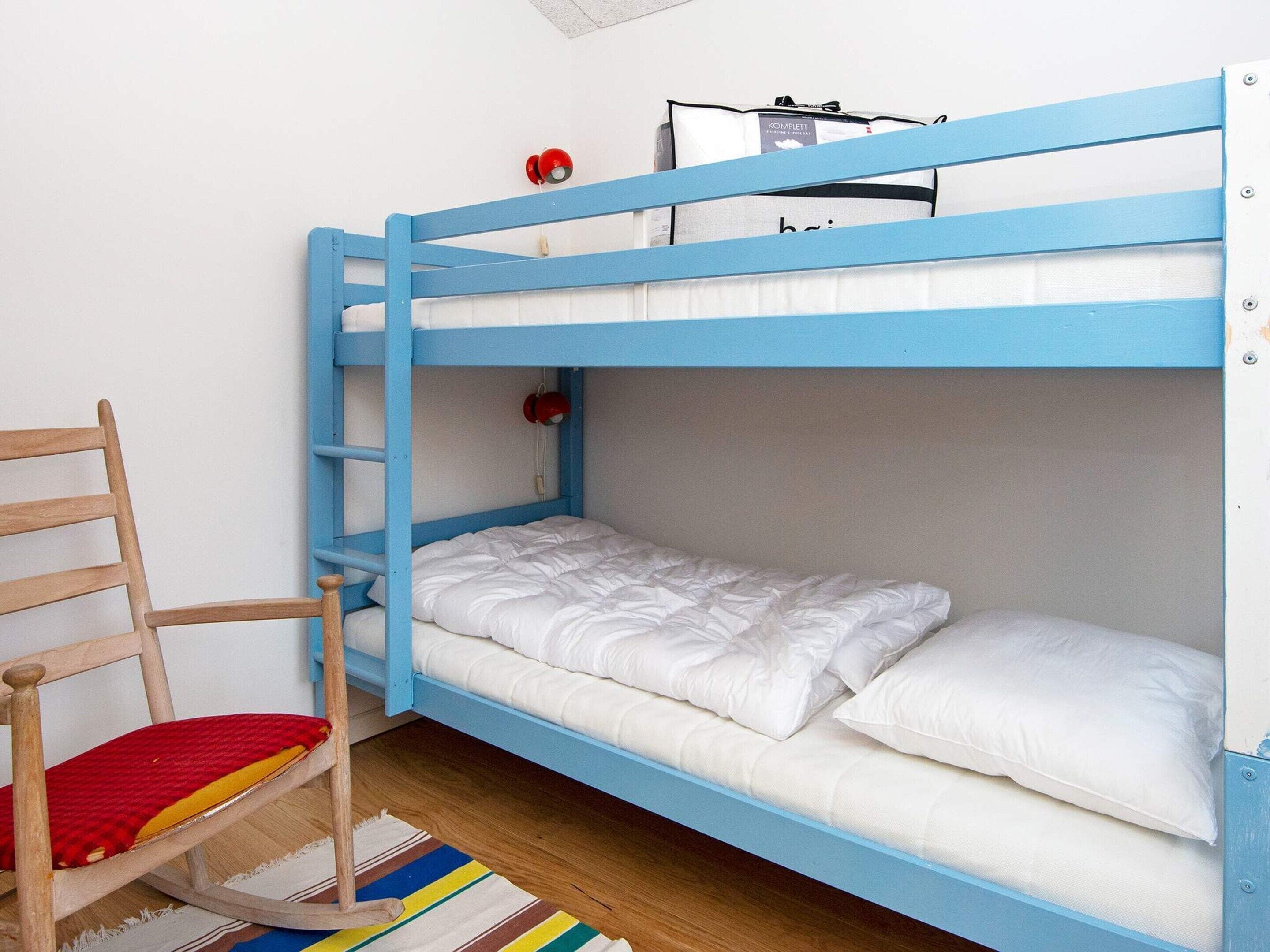 A bunk bed with a wooden chair and a striped rug.