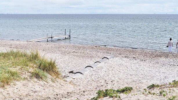 Una spiaggia con una battigia sabbiosa, un molo di legno e una persona in piedi vicino all'acqua.