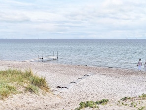 A beach with a sandy shore, a wooden pier, and a person standing by the water. - 5 Star Holiday Home in Sydals (Sydals)