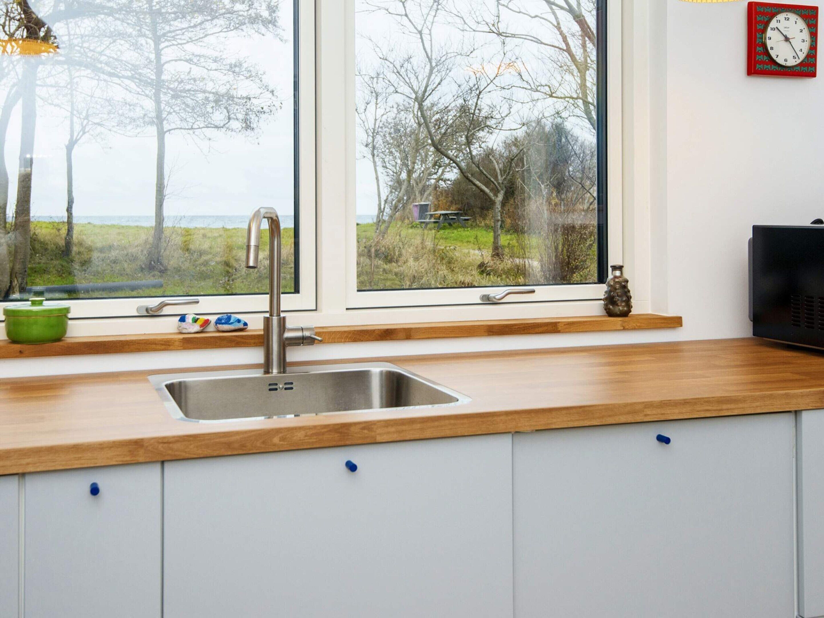 Eine Küche mit Spüle aus Edelstahl, einer Holzausziehtafel und Blick ins Freie durch große Fenster.
