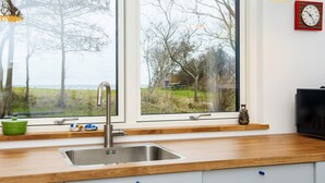 Una cucina con lavandino in acciaio inossidabile, piano di lavoro in legno e vista sull'esterno tramite ampie finestre.