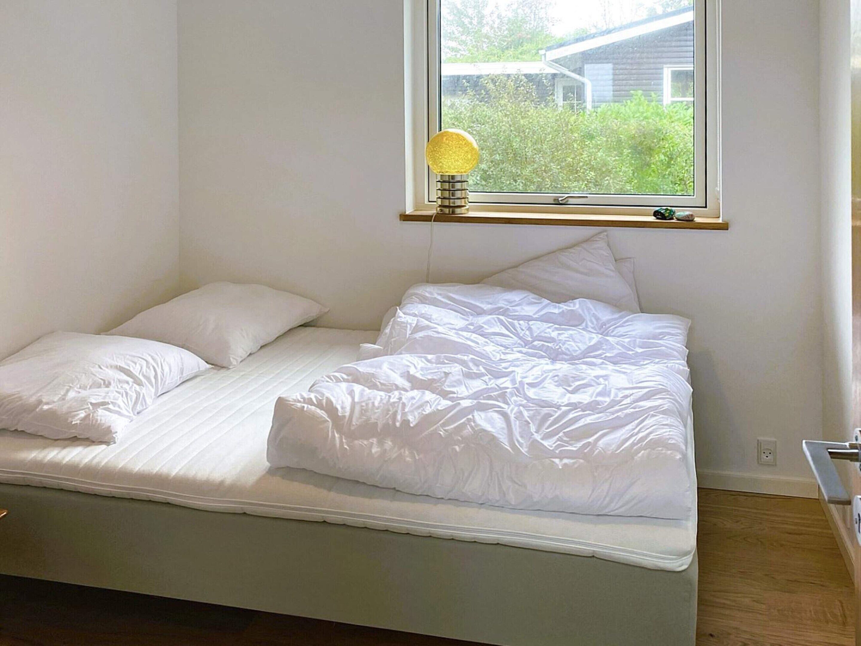 A single bed with white bedding in a room with a window.