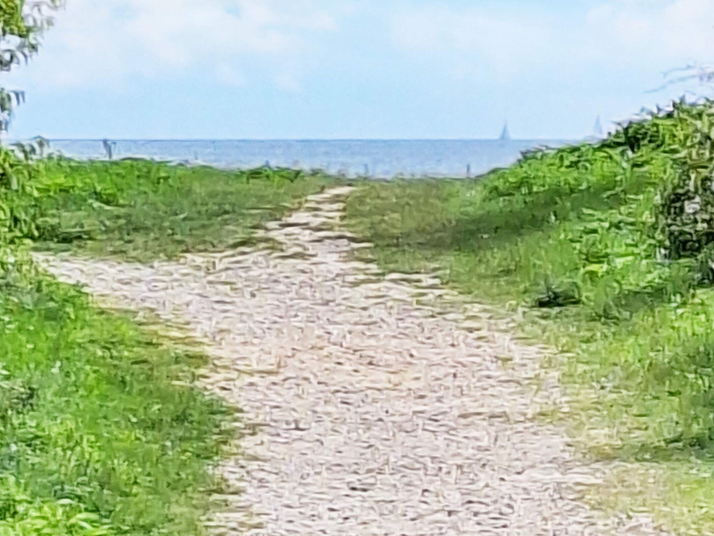 Un sentier de gravier mène à un plan d’eau, d’où l’on aperçoit au loin un voilier.