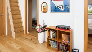 Una stanza con una scala in legno, una libreria con libri e un vaso di fiori, e un quadro appeso al muro.