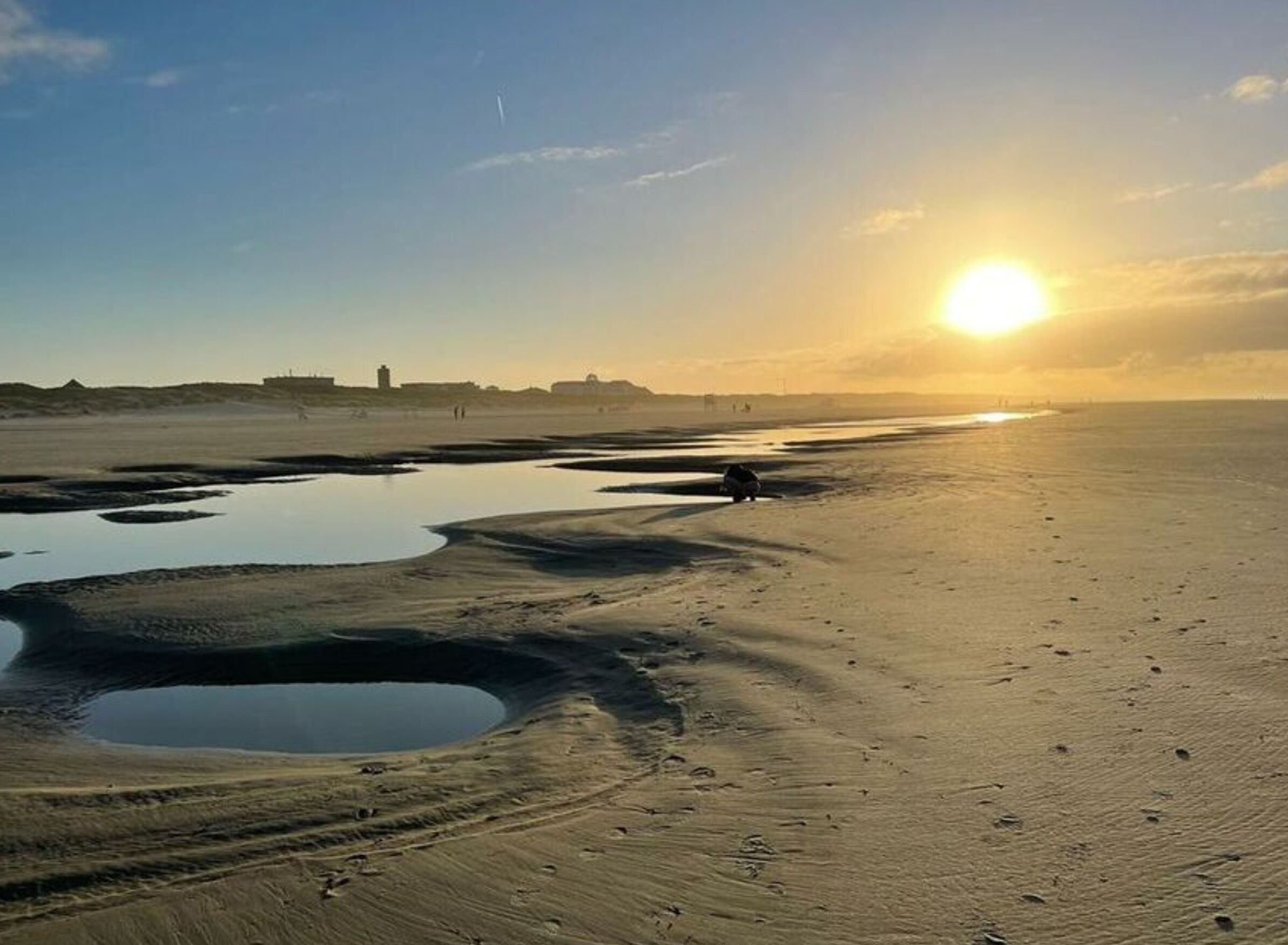 Een strand met waterpoelen en een ondergaande zon.