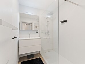 Ein modernes Badezimmer mit einer Duschkabine aus Glas, einem weißen Waschtisch und einem großen Spiegel.