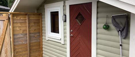 Une terrasse en bois, une porte rouge, une fenêtre et une moustiquaire.