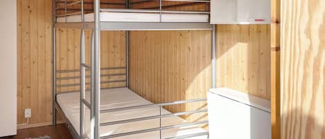 Una cama litera con estructura metálica y ropa de cama blanca, una pared de madera y un armario blanco con etiqueta roja.