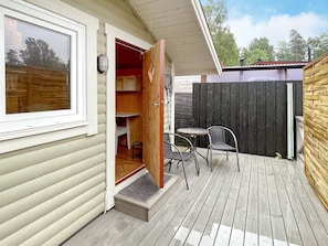 En träveranda med ett litet bord och några stolar, en dörr som leder in till ett rum, och utsikt över omgivningen.
